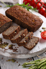 Healthy food. Sliced dark bread with pumpkin seeds and flax seeds on a white wooden board. Red cherry tomatoes, arugula on a light wooden background. Background image, copy space