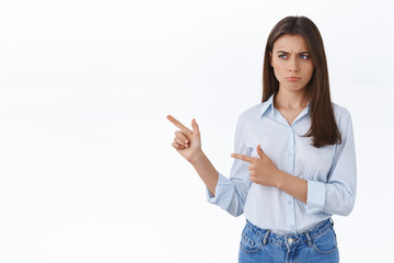 Upset or jealous cute brunette woman in blouse pouting, sulking with regret, being offended not invited to cool office party, squinting and looking pointing left with disapproval, white background