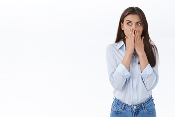 Astonished and shocked young woman overheard shocking information, gossiping at office, cover mouth with hands as gasping from amazement, look left startled, white background