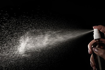 The hand presses the button of the aerosol dispenser. Water jet on a black background