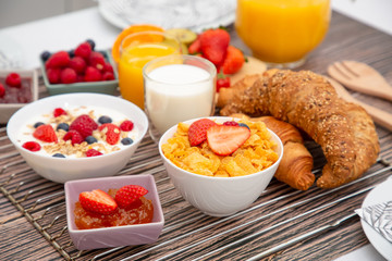 Breakfast Served in the morning with Fruit Yogurt, Butter croissant and corn flakes Whole grains and raisins with milk in cups and Strawberry, Raspberry, Kiwi, Fresh Orange Juice on breakfast table