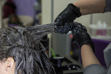 Professional hairdresser putting color mask dyeing hair of woman in beauty salon. Coloring hair spa and care procedures