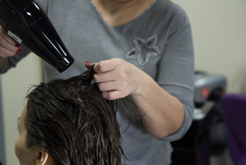 Professional hairdresser drying woman's hair with hair dryer in beauty salon after beauty procedures and hair coloring