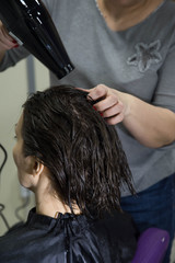 Naklejka premium Professional hairdresser drying woman's hair with hair dryer in beauty salon after beauty procedures and hair coloring