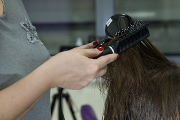Professional hairdresser drying woman's hair with hair dryer in beauty salon after beauty procedures and hair coloring