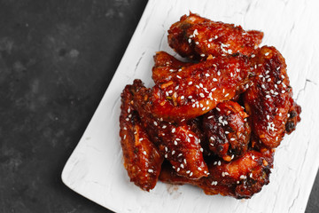 Grilled chicken wings in barbecue sauce with sesame and parsley on a wooden Board on a dark table. Top view with space for text. Delicious beer appetizer on a dark background.