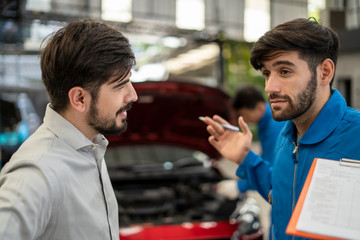 The mechanic in the blue jumpsuit is checking the engine in front of the red open car trunk and the...