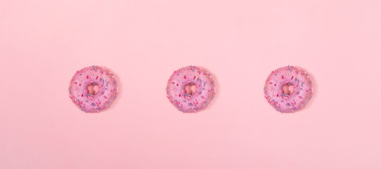 Creative minimal banner with doughnuts. Row of three traditional doughnuts with lilac glaze on trendy pink background. Top view, flat lay, copy space.