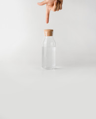 A hand points a finger at a glass bottle of clean water.
