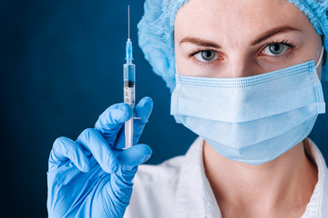 woman doctor dressed in a mask holds a syringe with a vaccine