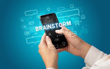 Female hand typing on smartphone with BRAINSTORM inscription, social media concept