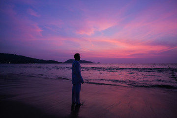 A man practices yoga on the ocean during a purple sunset.