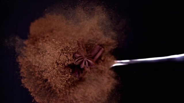 A Full Spoon Of exotic Christmas spice cinnamon anise and nutmeg falling down  on black background closeup in super slow motion