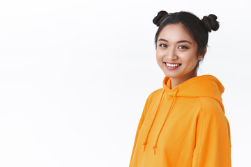 Close-up portrait young teenage asian girl with cute two hairbuns, wear orange hoodie, standing half-turned against white background near blank empty space for advertisement