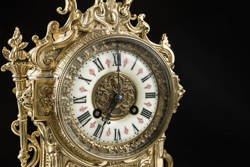 dial of vintage bronze clock on black background, antique clock photo close up, old bronze clock in gilding,  seven o'clock on the dial 