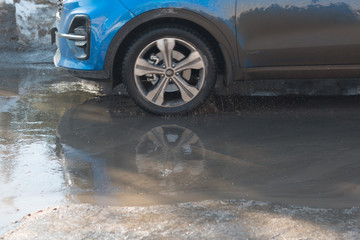 Vehicle car rides through spring puddles from melted snow. Spray from under the wheels.