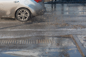 Vehicle car rides through spring puddles from melted snow. Spray from under the wheels.