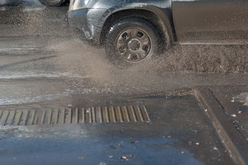 Vehicle car rides through spring puddles from melted snow. Spray from under the wheels.
