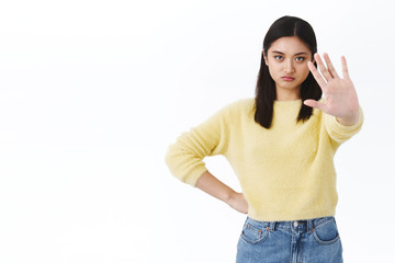 Skeptical and confident, serious asian girl stretch hand forward in stop sign, frowning and...