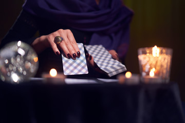 Close-up of woman fortuneteller's hands with cards at table with candles, magic ball in dark room