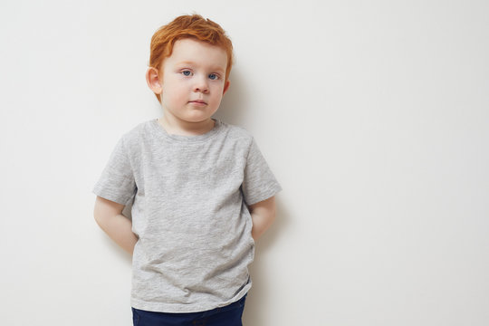 Portrait of redhead boy standing agianst a white wall