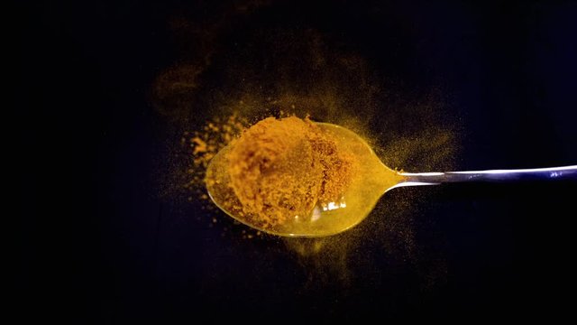 A Full Spoon Of exotic spice turmeric Flying up and Falling down on black background closeup in super slow Moti