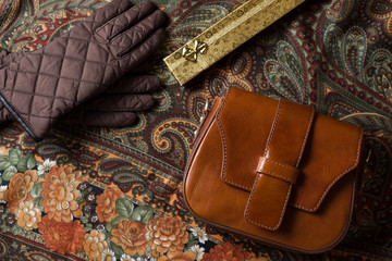 brown leather vintage bag on background with flowers and abstract patterns, brown gloves and vintage leather bag top view, ladies leather bag with brown gloves and a gold gift box