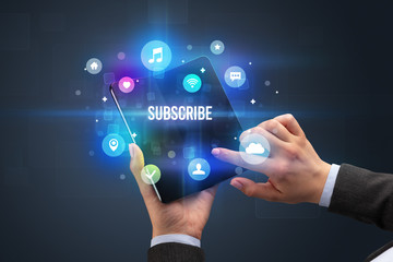 Businessman holding a foldable smartphone with SUBSCRIBE inscription, social media concept