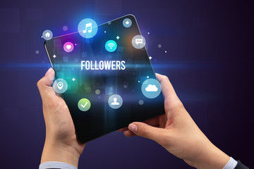 Businessman holding a foldable smartphone with FOLLOWERS inscription, social media concept