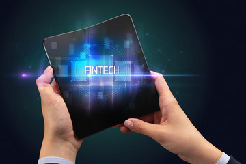 Businessman holding a foldable smartphone with FINTECH inscription, new technology concept