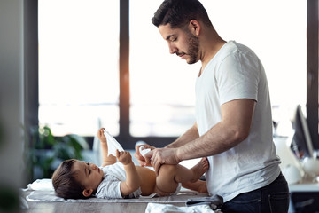 Concentrated young father changing the nappy to his little baby at home.