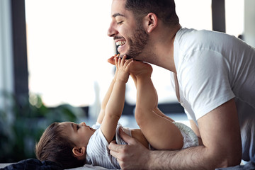 Smiling young father has fun with little baby while changing his nappy at home.