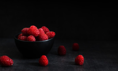 red raspberry in a black bowl on a dark background.