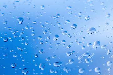 Wet glass with rain drops on blue sky background_