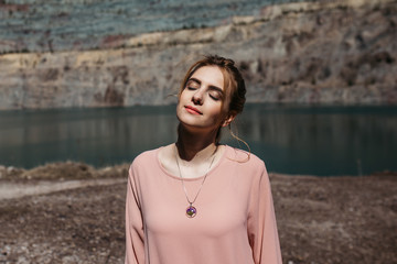 Outdoor portrait of woman wearing purple handmade floral necklaces and pastel dress- beauty and jewellery concept. Wind is playing with her hair.