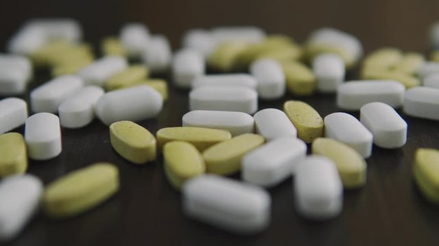 Yellow and white pills on the table, slowly approaching focus on macro close up