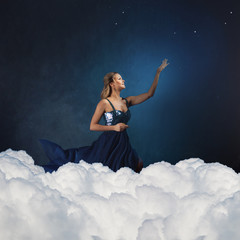 romantic young woman in a blue dress against a blue sky pulls her hand up.