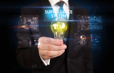 Fototapeta na wymiar Businessman holding lightbulb with SURVEILLANCE SYSTEM inscription, online security idea concept