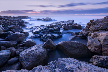 A pre-dawn photograph of misty waves crashing on the rocks by the South Coast in South Africa