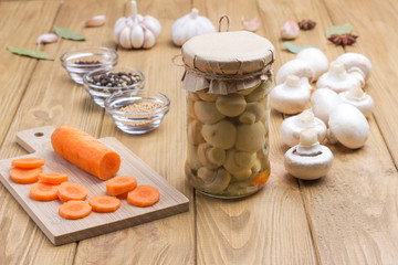 Glass jar with canned mushrooms. Spice: solt, garlic, onion, bay leaf on table