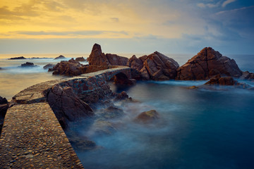 Pequeña pasarela en el mar al amanecer hasta un conjunto de rocas