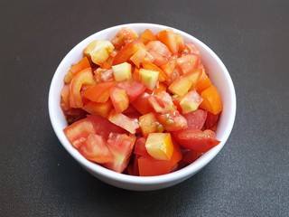 Top view of tomatoes sliced in white bowl isolated on dark background (Solanum lycopersicum var. cerasiforme), Ready to eat or cooking