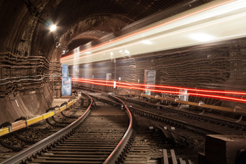 A passing train the lights of the metro tunnel.At the intersection of two metro lines.Goes into the tunnel.With red lines