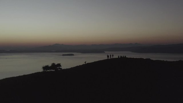 Silhouette of a group of people taking photos on a hill top with late Sunset light over Padar island and bay, Indonesia, Aerial follow footage.