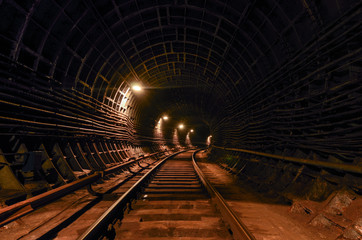 A lighted reinforced concrete subway tunnel, cable routes are laid, the railroad tracks turn left. In front of them are iron vertical boxes of automatics.