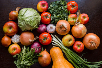 onions, garlic, tomato, greens, parsley, arugula, cabbage, apples, beetroot, carrots, pumpkin, lie on a wooden table