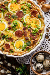 Easter Quiche tart with eggs and sausage sprinkled with fresh chive on a festive table, view from above close-up