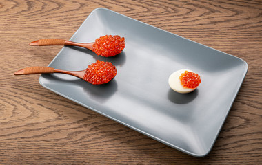 Red caviar in an egg , and wooden spoons in a gray rectangular plate