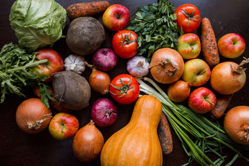 onions, garlic, tomato, greens, parsley, arugula, cabbage, apples, beetroot, carrots, pumpkin, lie on a wooden table