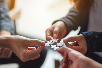 Closeup image of a group of people holding and putting a piece of white jigsaw puzzle together